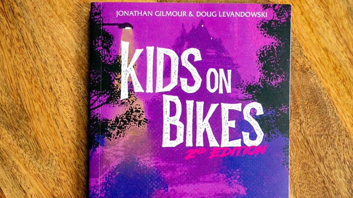 A screenshot of a physical copy of Kids on Bikes Second Edition on a wooden background